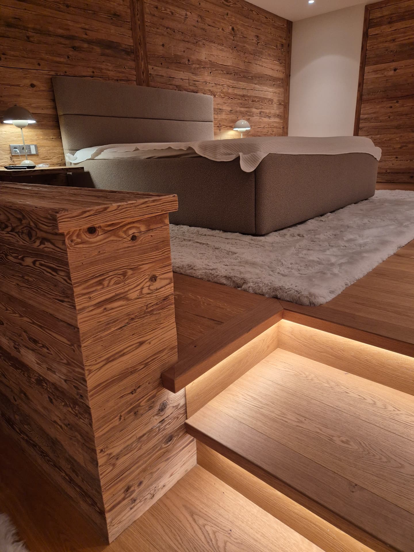 Schlafzimmer mit Altholzwand und beleuchteter Stufe
